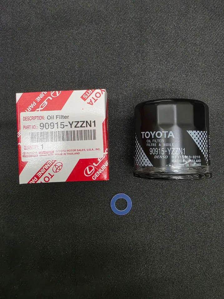 A Toyota engine oil filter with its red and white original packaging box and a blue gasket, displayed on a dark textured surface.